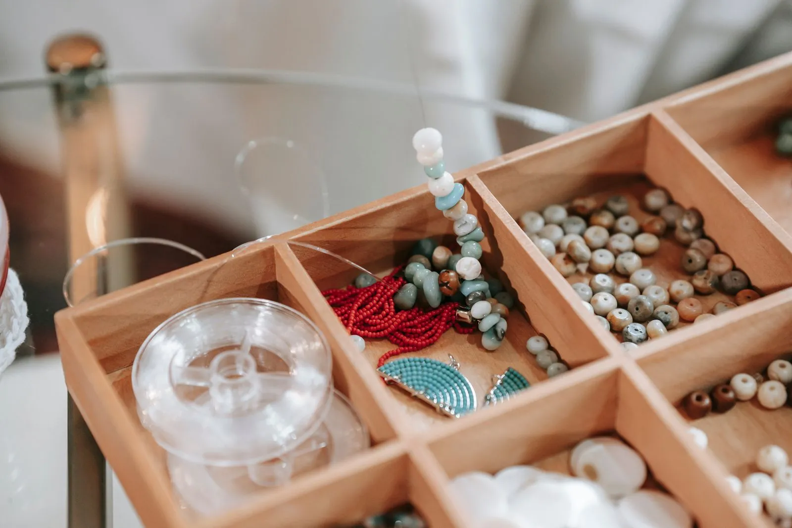 Wooden container with abundance of colorful beads and elastic cord for making bracelet placed on glass table in light room